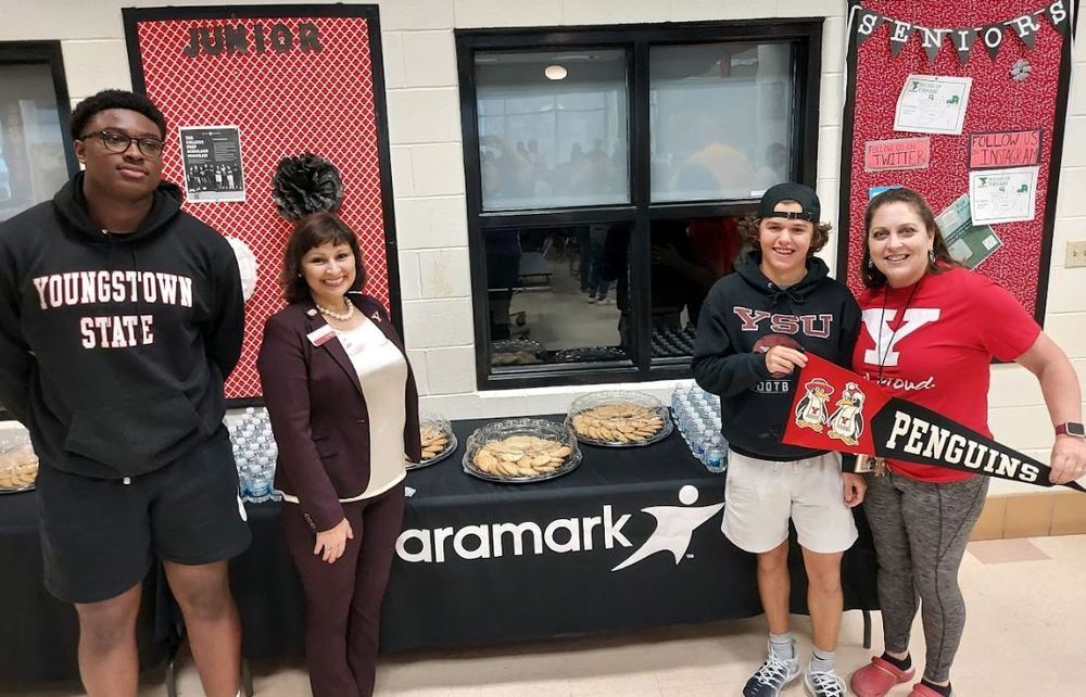 Students, Alumni and Youngstown State University Rep pose in front of Aramark reception table for E3 event 